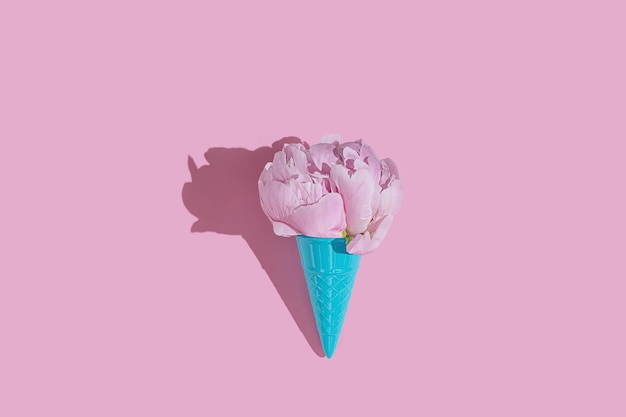 Creative blue toy ice cream cone with pink peony fluffy flower on pink minimal background with copy space flat lay Botany idea for summer or spring wallpaper or greeting card