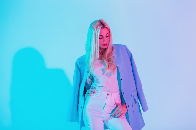 Creative bright portrait of a beautiful young woman in a fashionable blue blazer with white clothes with pastel colors neon pink lights in the studio