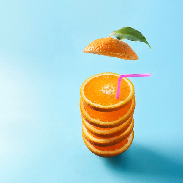 Creative colorful summer concept on a blue background Falling sliced oranges in the shape of a cocktail with a straw