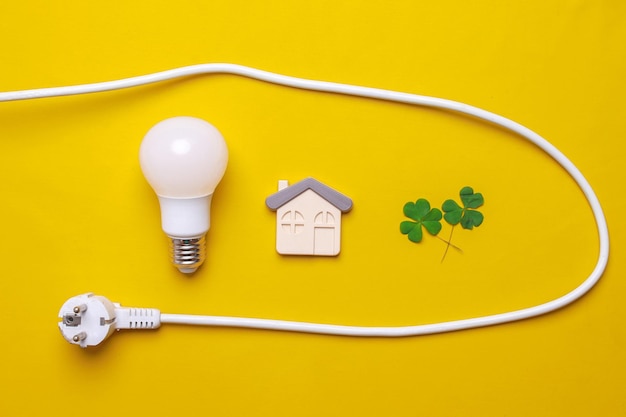 Creative composition of house symbol with electric plug plant and light bulb on yellow background