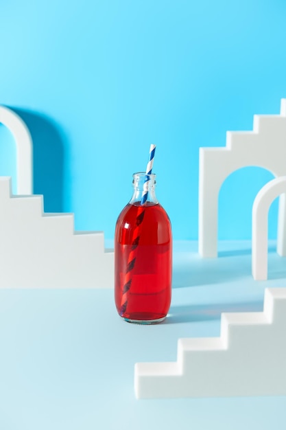 Creative composition with cranberrie lemonade cocktail in bottle on blue background