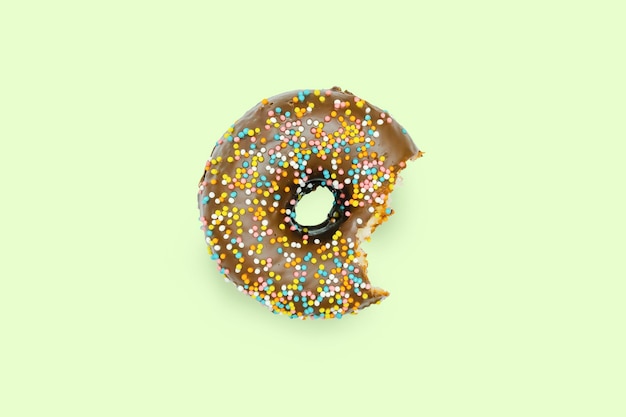 Photo creative concept of biting eating delicious sweet sugar brown black doughnut donut with glaze on green background top view flat lay unhealthy junk dessert food concept mock up copy space