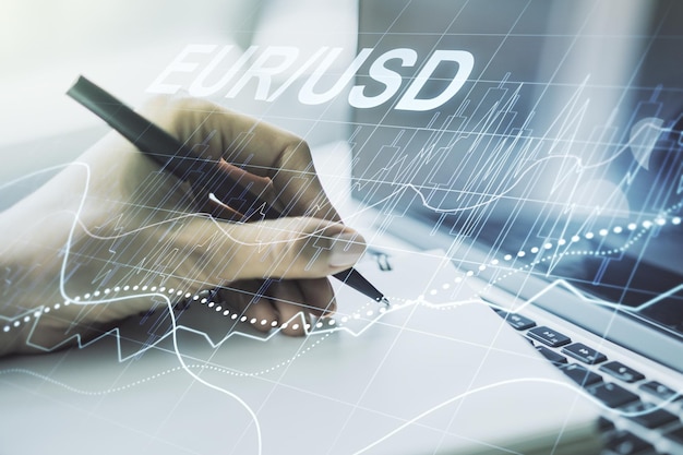 Creative concept of EURO USD financial chart illustration and hand writing in notebook on background with laptop Trading and currency concept Multiexposure