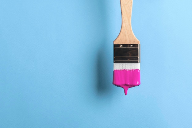 Creative concept of repair Paintbrush with dripping purple paint on blue background with copy space