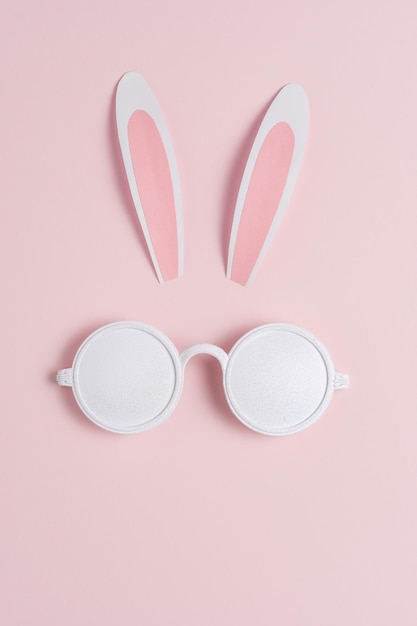 Creative Easter concept with bunny ears and white sunglasses on pink background Minimal Easter concept