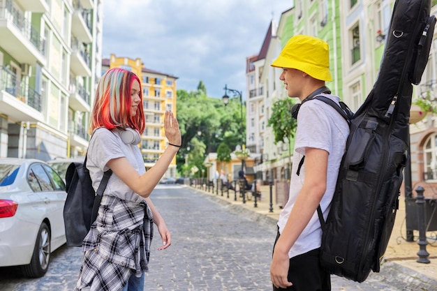 Creative fashionable youth Talking guy with guitar in case and beautiful girl with trendy dyed colored hair city street background