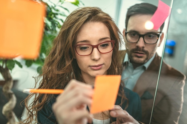 Creative female professionals executive are standing at the office behind glass wall with sticky notes.