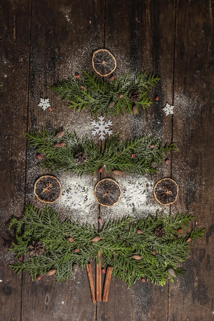 Creative fir tree from evergreen branches, dried lemon slices and snowflakes. Wooden background, flat lay, festive decor, top view