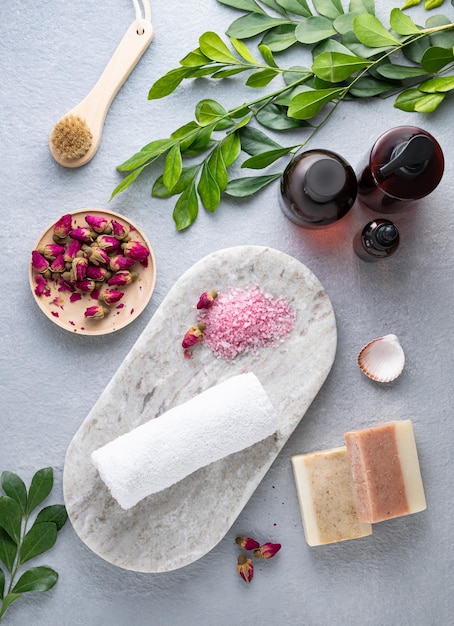 Creative flat lay of facial and body care cosmetics with sea salt soap cream and brush on blue background Top view