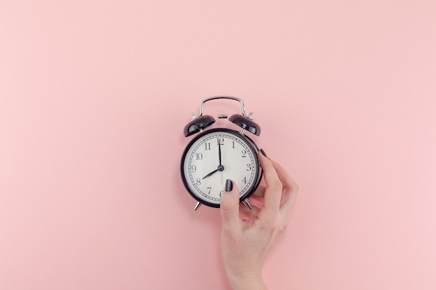 Creative flat lay morning time emotions concept top view of woman hand holding black vintage alarm clock