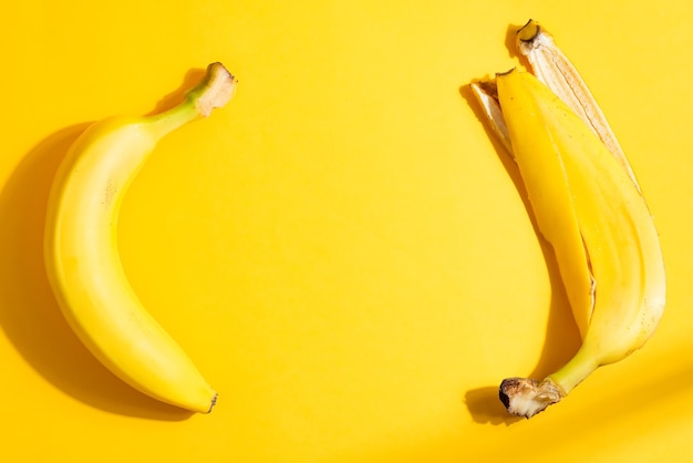 Creative fruits frame from ripe fresh yellow banana and peel on the same color background with hard shadows, copy space. Top view. Vegetarian healthy food concept.