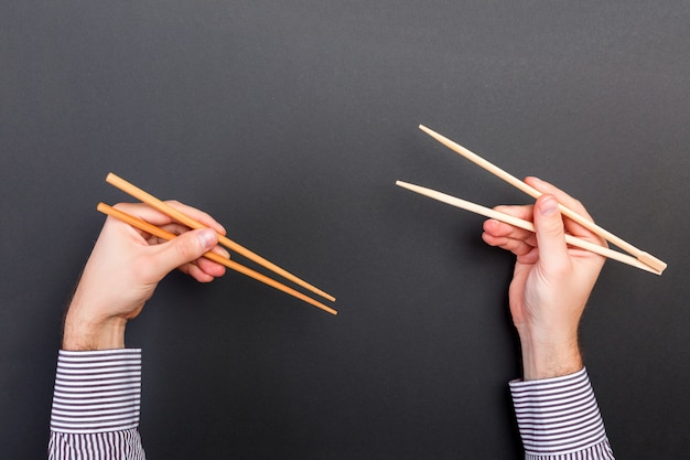 Creative image of wooden chopsticks in two male hands on black