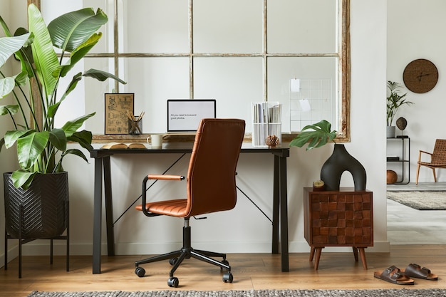 Creative interior composition of modern masculine home office workspace design with black industrial desk, brown leather armchair, laptop and stylish personal accessories. Template.