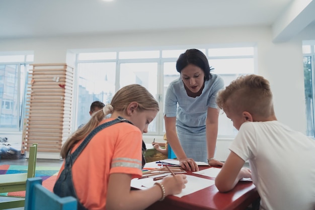 Creative kids during an art class in a daycare center or elementary school classroom drawing with female teacher