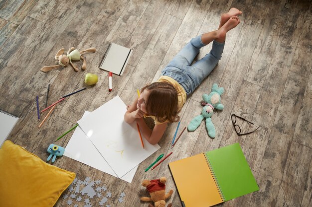 Creative kids concept top view of little caucasian girl lying on the wooden floor at home and