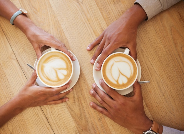 Creative latte art cappuccino and coffee drink in cafe with couple and friends enjoying cup of java with milk froth together Closeup of people hands from above meeting and drinking in restaurant