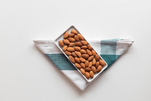 Photo creative layout made of fresh nut almonds in a ceramic bowl with a towel