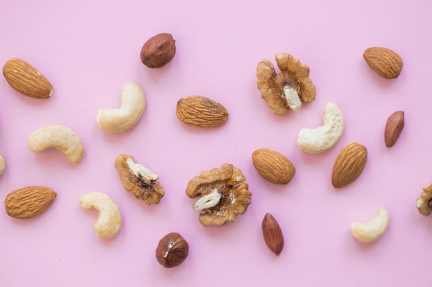 Creative layout made of hazelnut nuts almonds walnut peanut cashew on pink background Flat lay