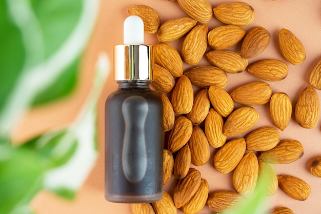 Photo creative layout natural almond oil in a matte glass bottle and scattering of almonds on a pastel