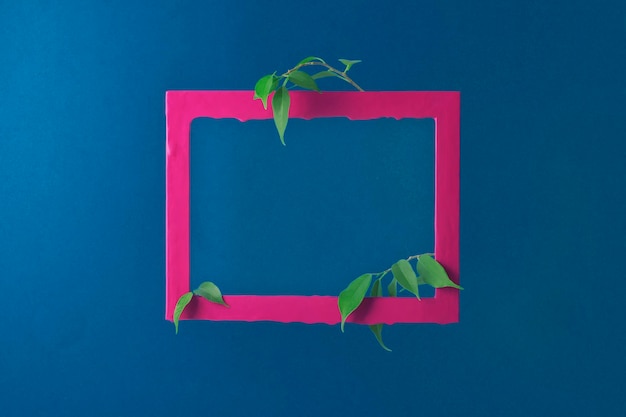 Creative layout of a pink rectangular frame and branches with leaves on a dark blue background