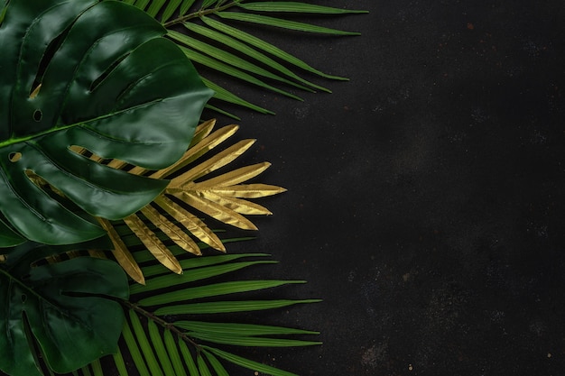 Creative layout with gold and green tropical palm leaves on black background