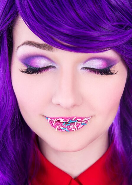 Creative makeup - young beautiful woman with purple hair and colorful sugar candies on lips