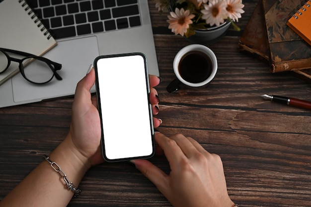 Creative man hands holding smart phone with blank screen on wooden desk