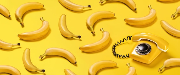 Creative pattern bananas and old yellow phone with hard shadows pattern on yellow background flat lay banana phone horizontal banner