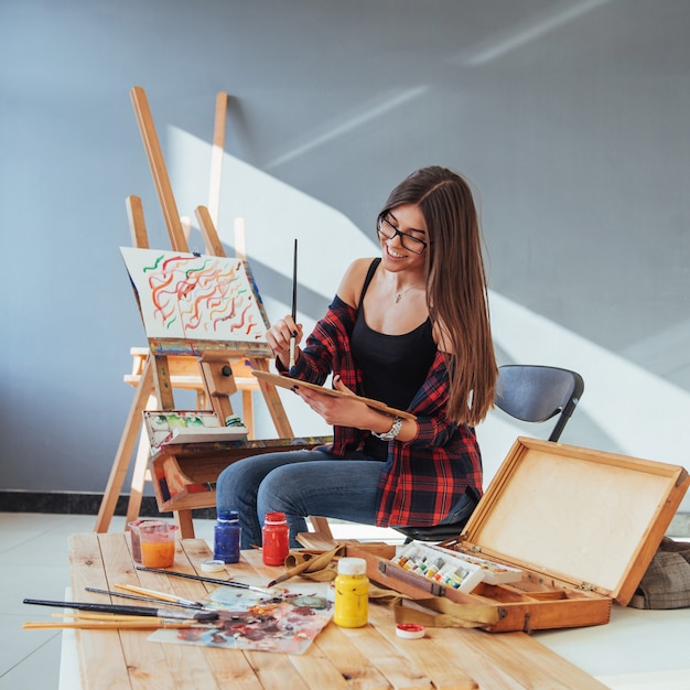 Creative pensive painter girl paints a colorful picture on canvas with oil colors in workshop