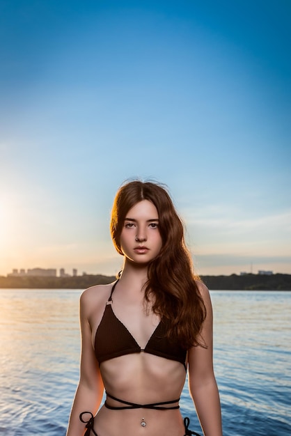 Creative portrait of a brunette in a black swimsuit Design concept Romantic portrait of a young woman relaxing against the backdrop of sunset