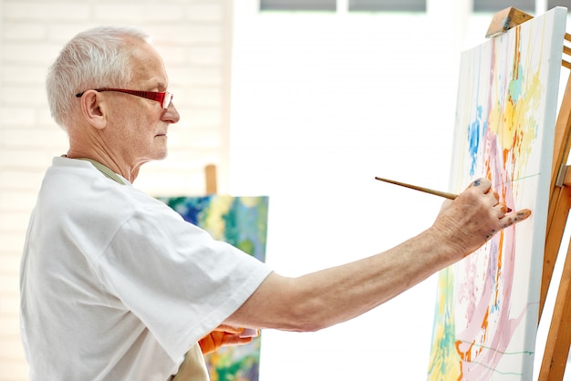 Creative senior painter drawing colorful picture at bright studio. 