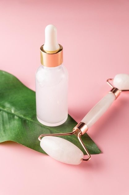 Creative shot of pink jade roller and serum bottle on pink background. Home skin care procedures. Copy space.