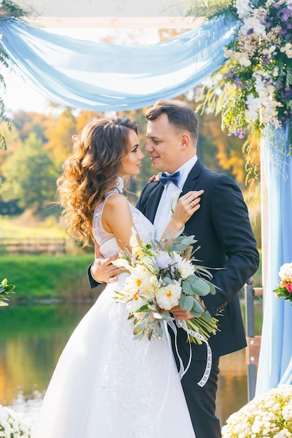 Creative stylish wedding ceremony elegant curly bride and groom outdoors on the background the lake