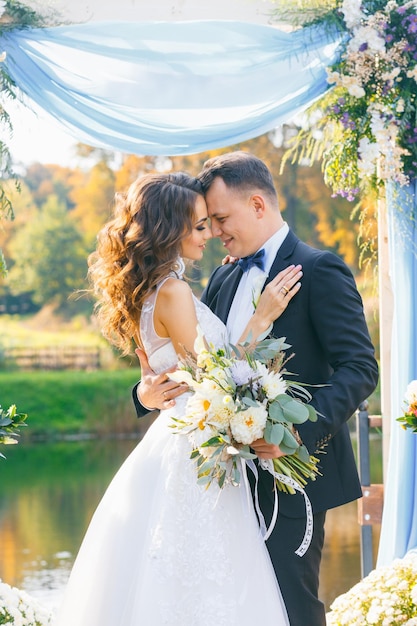 Creative stylish wedding ceremony elegant curly bride and groom outdoors on the background the lake