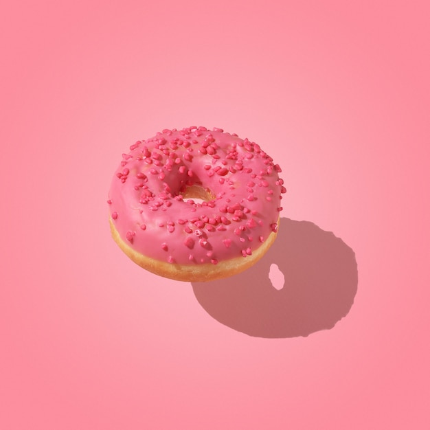 Creative sweet food concept. A pink donut floating above a pink background.