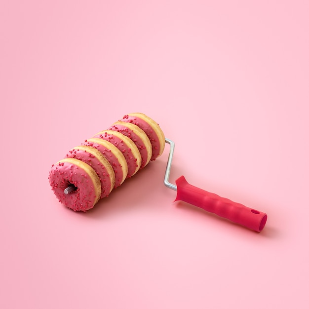 Creative sweet food concept with copy space. Paint roller with donuts on a pink background.