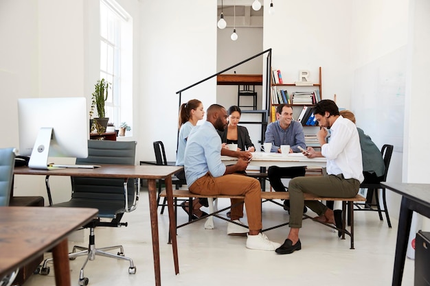 Creative team meet at a table in an office one using phone