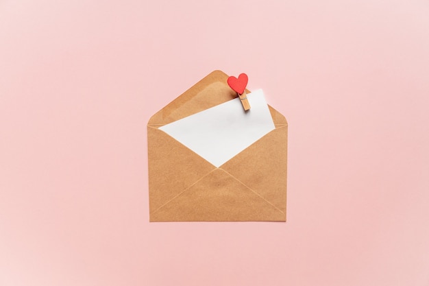 Creative Valentine Day romantic composition with paper envelope, red heart and gift box on pink.