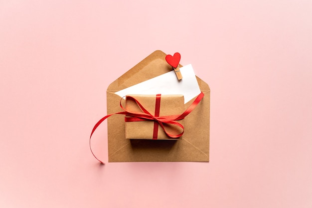 Creative Valentine Day romantic composition with paper envelope, red heart and gift box on pink