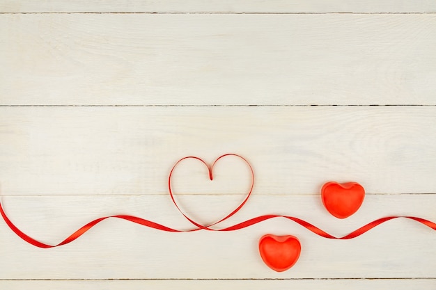 Creative Valentine Day romantic composition with red hearts, satin ribbon on wooden background. Mockup with copy space for blogs and social media.