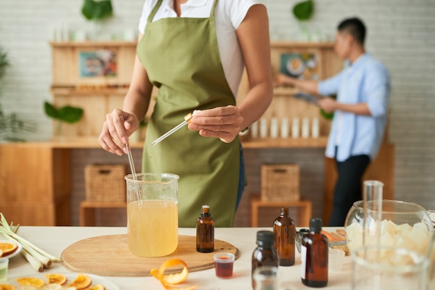 Creative woman mixing melted soap base with glass stick when adding few drops of essential oil