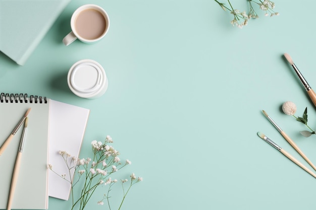 Photo a creative workspace setup with a cup of coffee notebooks paintbrushes and flowers