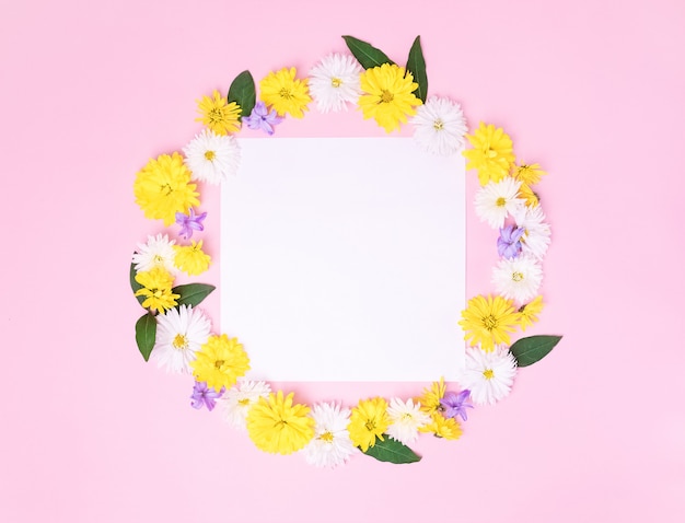 Creative wreath made with beautiful flowers on pastel pink background, and blank white greeting card