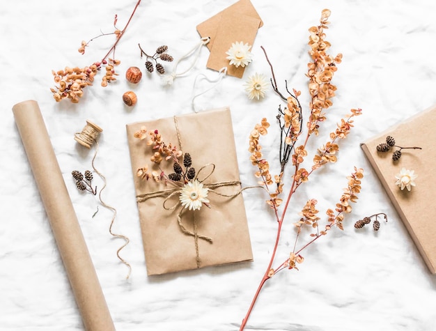 Creativity is a concept Autumn cozy cute gift packaging in craft paper with natural natural elements flowers cones twigs on a light background top view