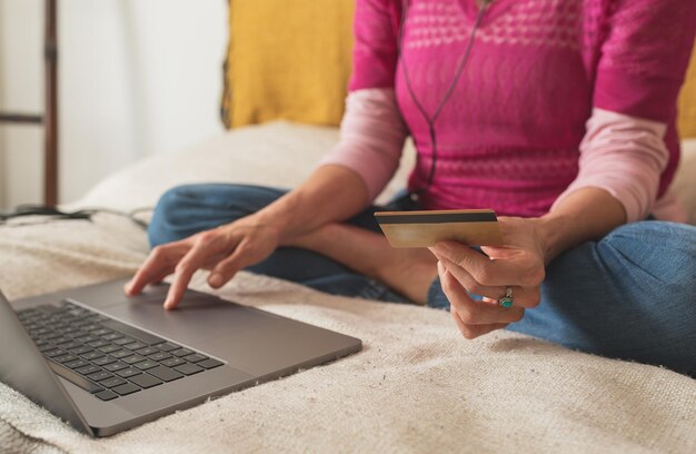 Credit card and female hand in the foreground, young woman sitting in front of her laptop makes online purchases,  concept of online music shopping