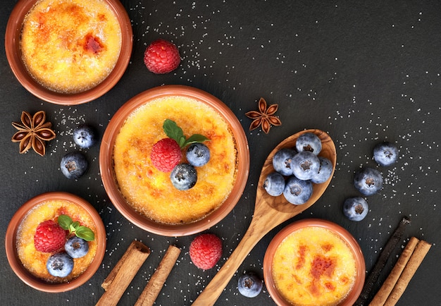 Creme brulee with berries and ingredients on dark stone, top view