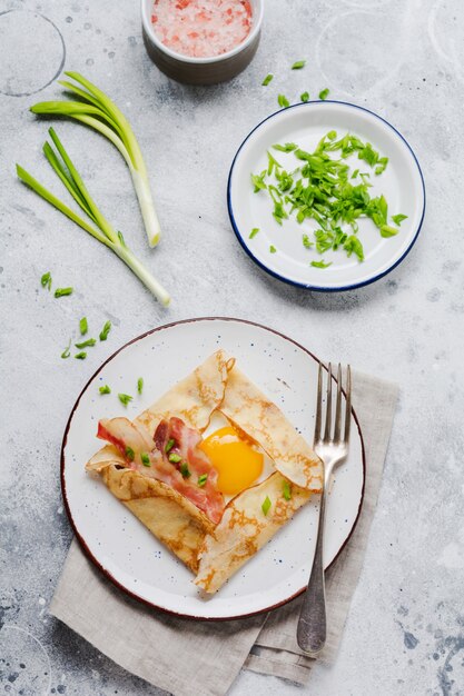 Crepe with fried egg, cheese, bacon and green onions for breakfast on a light gray concrete surface