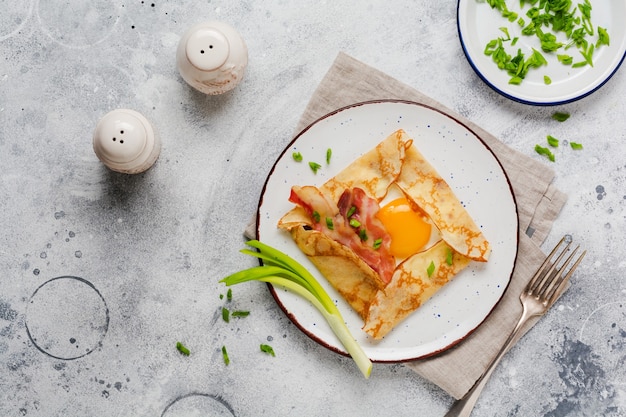 Crepe with fried egg, cheese, bacon and green onions for breakfast on a light gray concrete surface