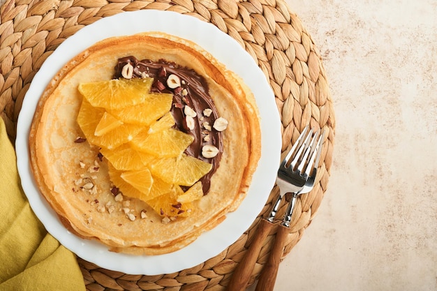 Crepes suzette with oranges Thin crepes with chocolate spread hazelnuts and orange slices fruit in white plate for breakfast on old concrete rustic table background Copy space Top view