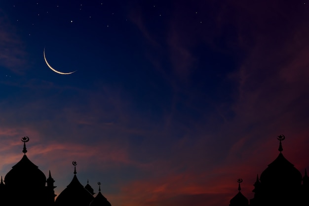 Crescent moon on dark blue dusk sky over mosques dome background